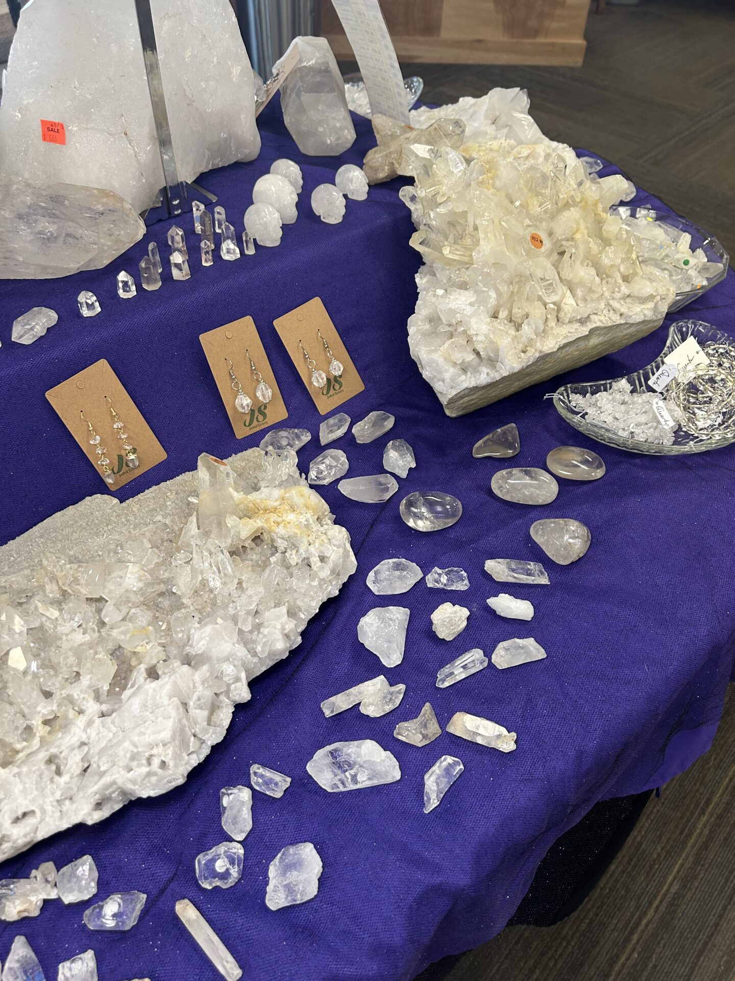 Clear Quartz sitting on a table with a purple tablecloth. There are large pieces and small pieces of clear quartz.