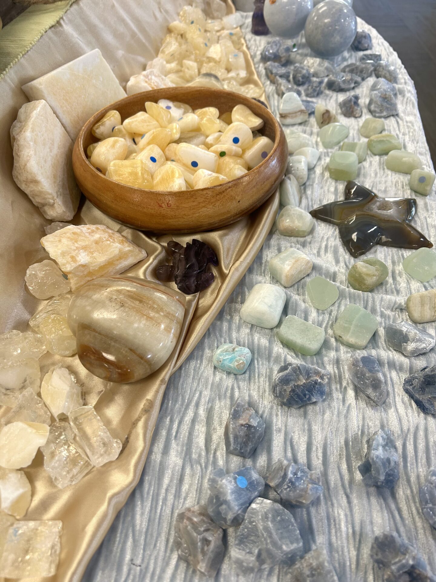 A table with calcite crystals on it. They are yellow, blue, and green. The table cloth is blue with a gold sheet partially on it.